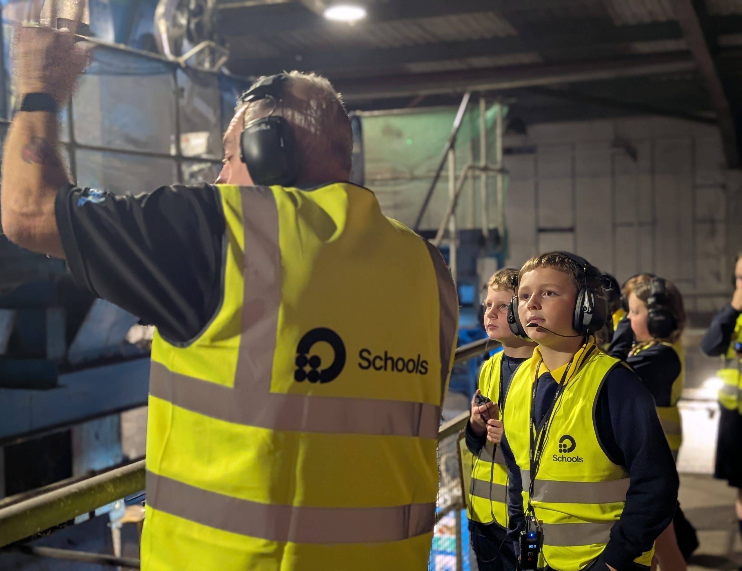 Wastesavers - An adult in a high-visibility vest gives a tour to a group of children wearing headsets in an industrial facility.
